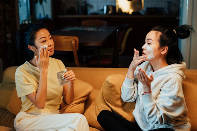 Two Asian women sitting oTwo Asian women sitting on a couch and applying face creamn a couch and applying face cream